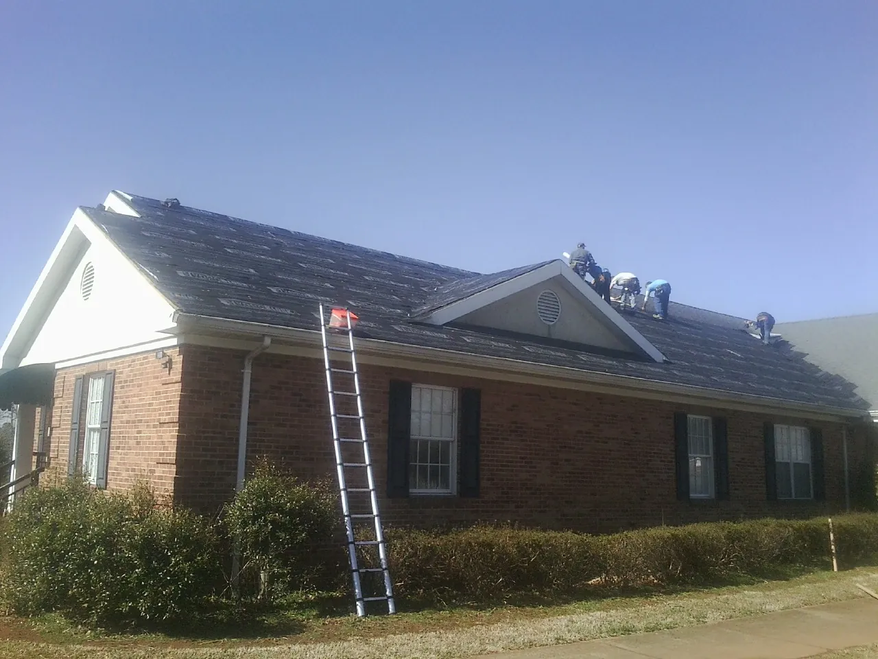 Crew tearing shingles off a brick ranch roof with a ladder set — Metal Roof Repair work by our crew in New London