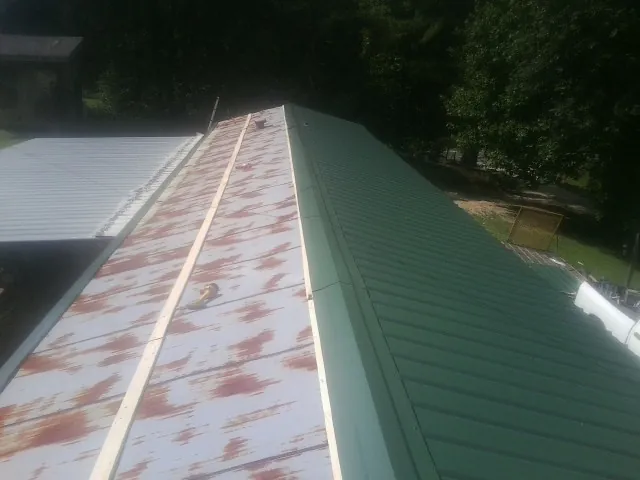 Old rusted panels beside newly installed green metal roofing — Wind Damage Roof Repair by Roofing Brothers in New London