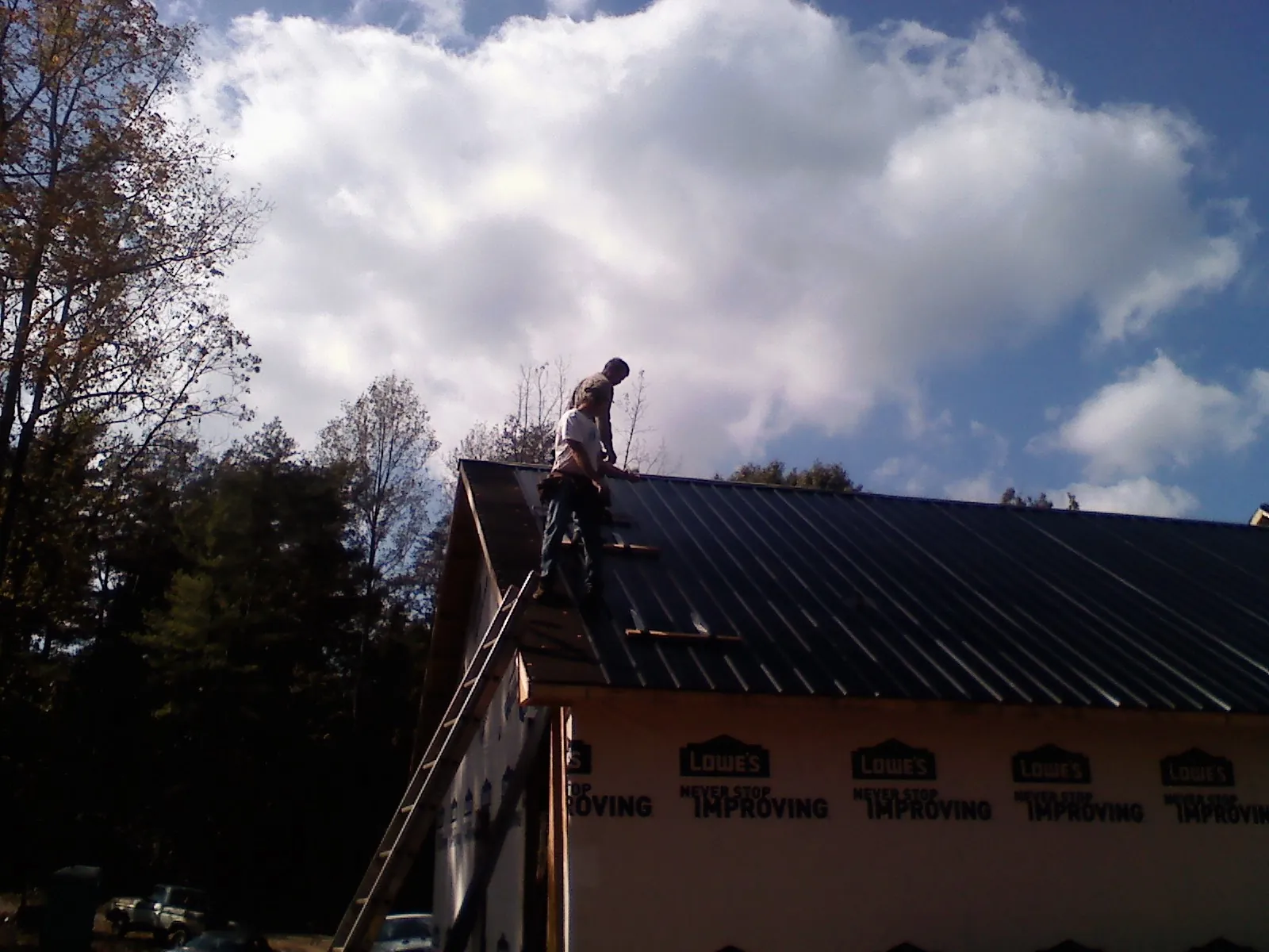 Roofer fastening dark metal panels high against a cloudy sky, from a Roof Inspection job in New London